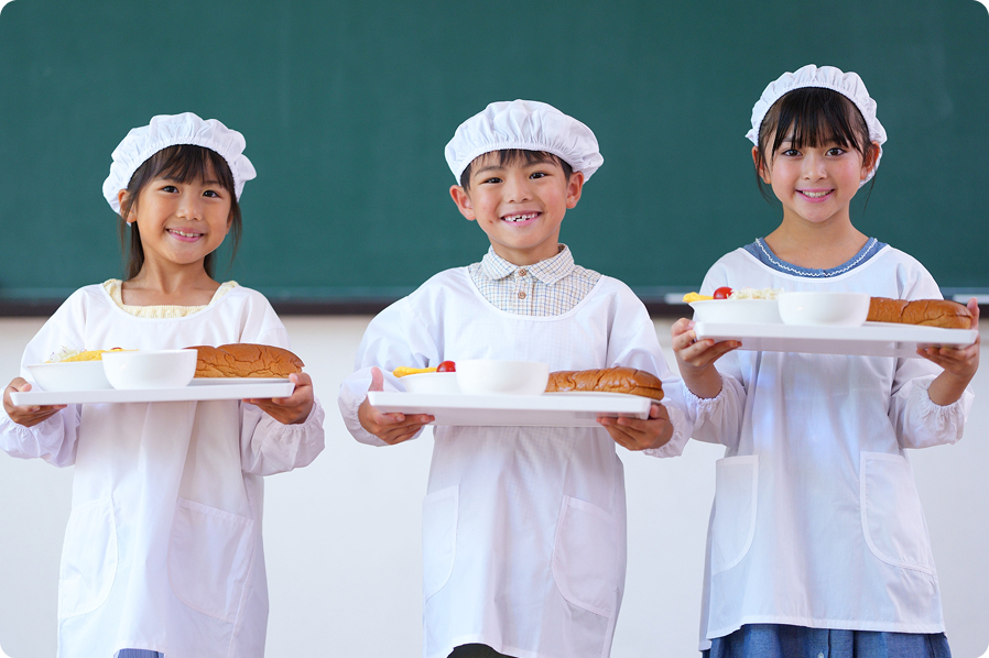 給食用白衣を着た子どもたちが食器を持っている